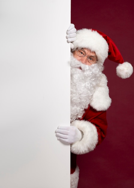 Il bello babbo natale emozionante felice sta proponendo e mostrando il bordo in bianco bianco nelle mani