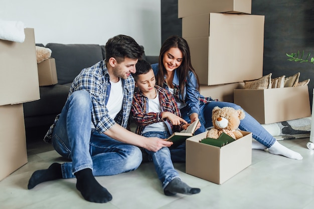 Beautiful happy family bout a house. Moving concept. Happy  couple with cardboard box and son reading a book