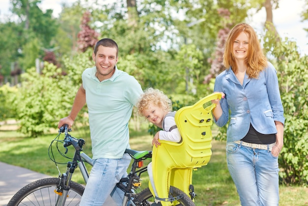Bella famiglia felice in bicicletta al parco con un bambino nel seggiolino per bici, trascorrendo del tempo insieme.