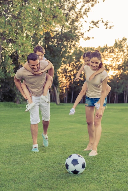 Beautiful happy family is smiling while playing soccer in park kids are riding piggyback