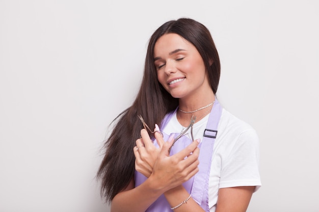 Beautiful happy female manicurist in apron smiling with eyes closed holding manicure tools