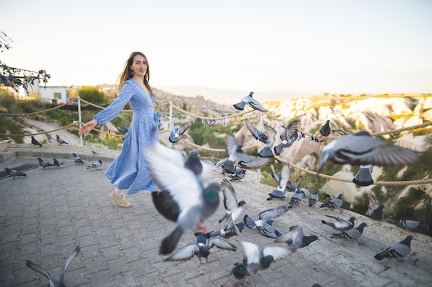 A beautiful and happy girl in a dress and many pigeons in the mountains of Cappadocia