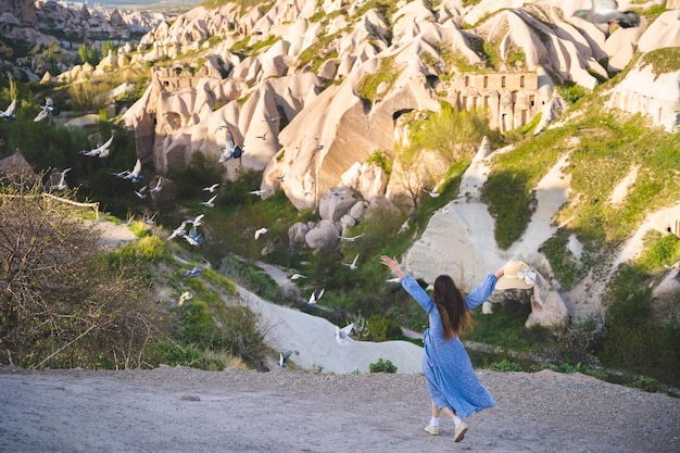 A beautiful and happy girl in a dress and many pigeons in the mountains of Cappadocia