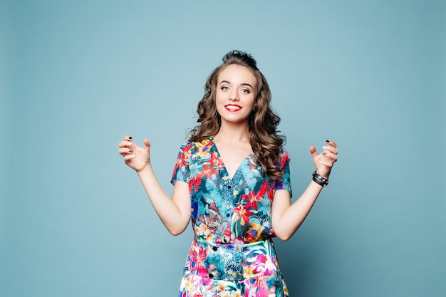 Beautiful happy girl in floral dress holding bottles over blue background.