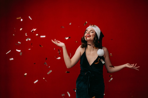 Beautiful happy girl in a santa hat throws confetti New year concept