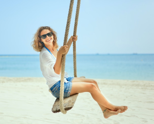 ビーチでブランコに乗って美しい幸せな女の子。休日、休暇、旅行