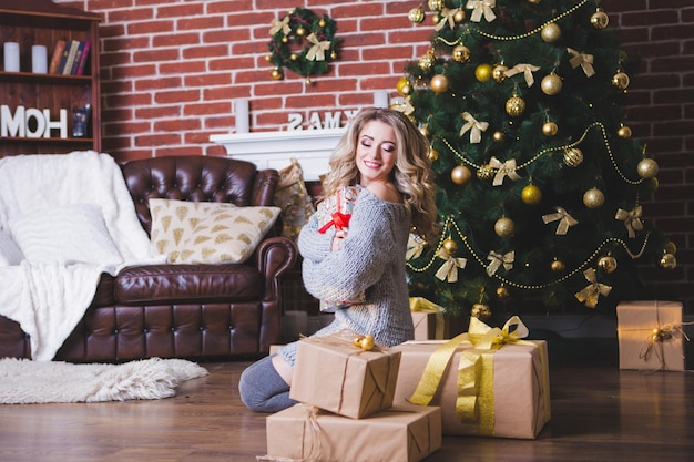 Beautiful happy girl unfolding a Christmas gift box on a holiday in the morning in a beautiful room room The girl is open a Christmas gift near the decorated Christmas tree Concept of winter holidays