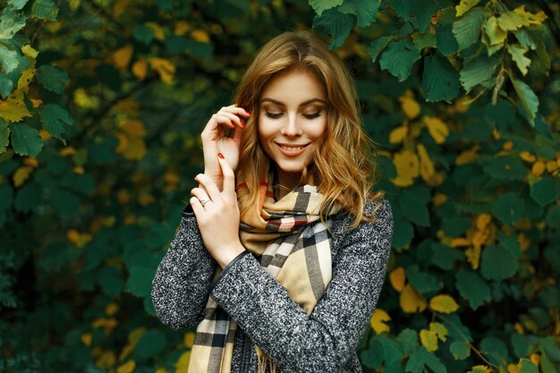 Beautiful happy girl in a vintage scarf and coat on a yellow-green foliage.