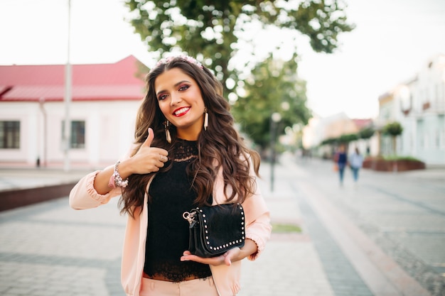 Beautiful happy girl with fashionable black handbag showing thumb up.