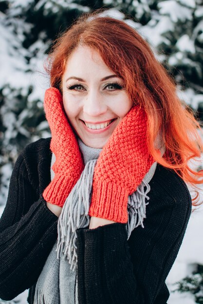 Beautiful happy girl with red hair in orange gloves on a background of a snowy forest