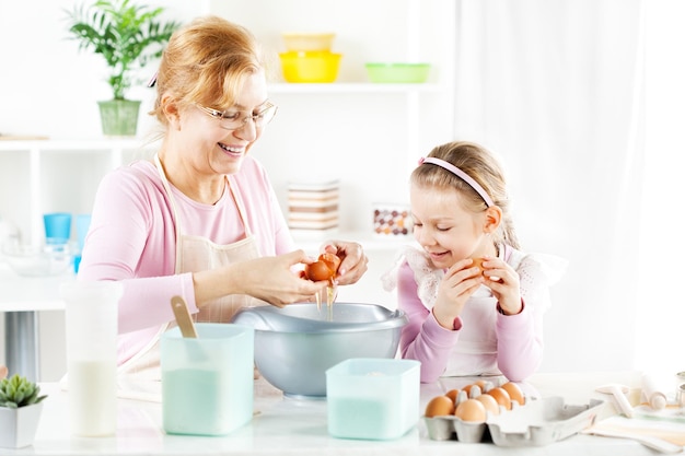 Beautiful happy grandmother and granddaughter making Dough in a kitchen.