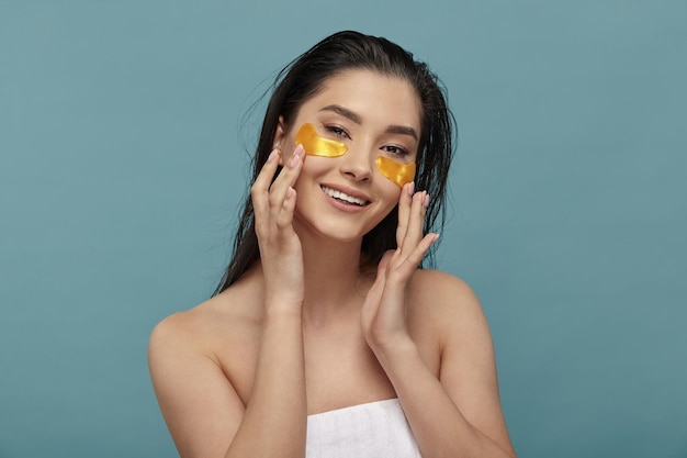 Beautiful happy lady using eye patches mask on blue