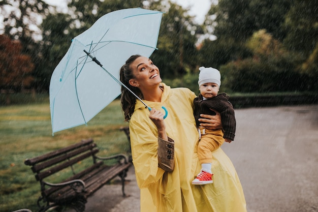 Beautiful and happy middle age woman with her baby walking in city park on rainy day.