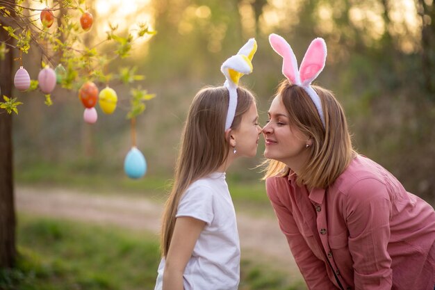 バニーの耳の美しくて幸せなママと娘はイースターエッグで木を飾りますイースターを祝う幸せな家族