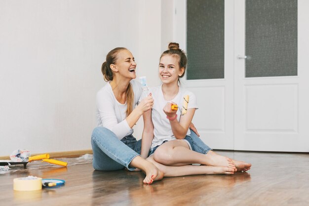 Photo beautiful and happy mom and daughter paint the walls in the apartment white