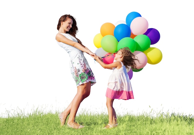 Beautiful happy mother with daughter having fun in green field holding colorful balloons