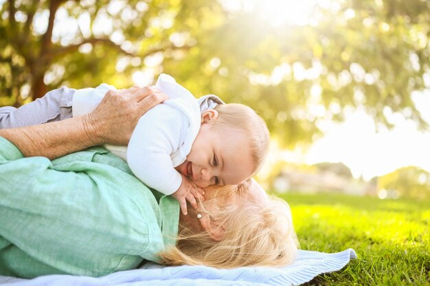 可愛い小さな男の子の祖母と一緒に草の上に横たわっている美しい幸せな笑顔の高齢の女性