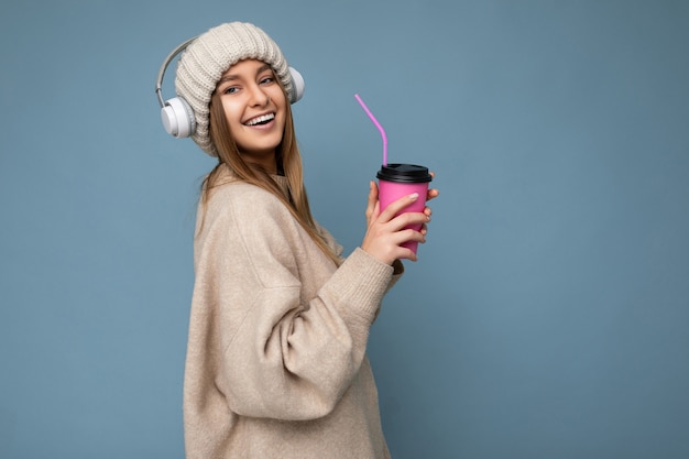 Bella giovane donna bionda sorridente felice che indossa un maglione invernale beige e cappello isolato