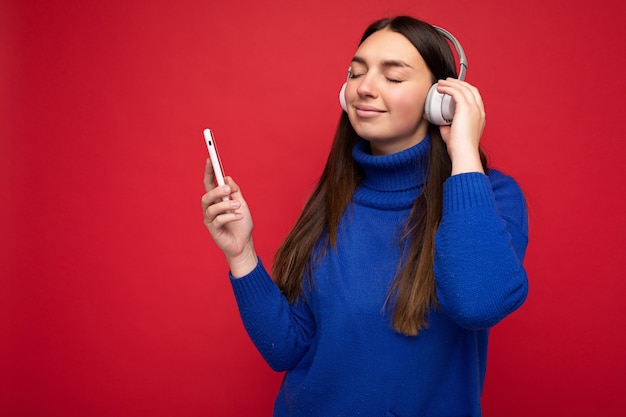 Bella sorridente giovane donna bruna che indossa un maglione blu isolato su sfondo rosso red