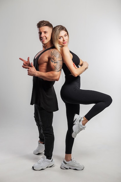 Beautiful happy sports couple in fashionable sportswear on a white background Handsome muscular man and beautiful fitness lady standing and posing in studio