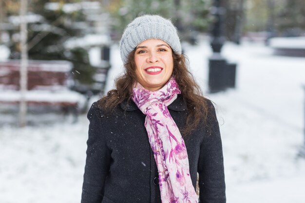 Beautiful happy woman dressed in black coat, pink scarf and grey hat