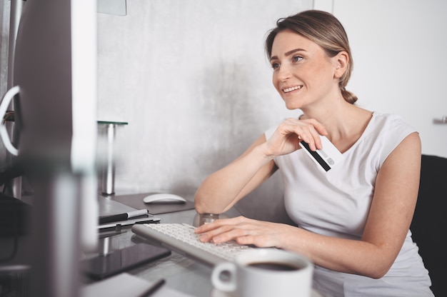 Beautiful happy woman holding credit card in hand and using laptop computer keyboard. Businesswoman or entrepreneur working. Online shopping, e-commerce, internet banking, spending money concept