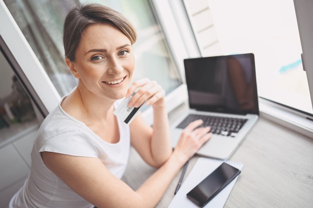 Photo beautiful happy woman holding credit card in hand and using laptop computer keyboard. businesswoman or entrepreneur working. online shopping, e-commerce, internet banking, spending money concept