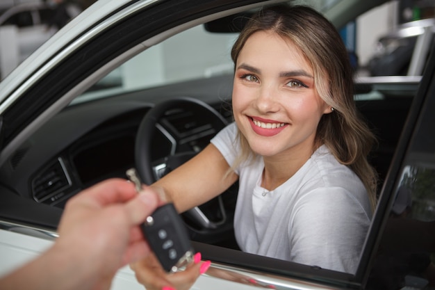 彼女の新しい自動車に座って、セールスマンから車のキーを受け取る美しい幸せな女性