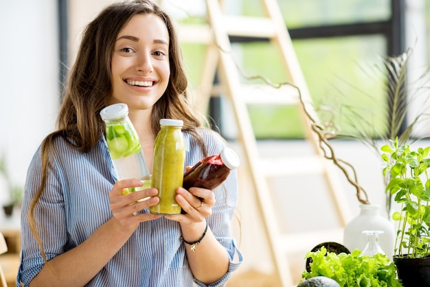 写真 家で飲み物と健康的な緑の食べ物と一緒に座っている美しい幸せな女性。ビーガンミールとデトックスのコンセプト