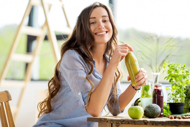 Bella donna felice seduta con bevande e cibo verde sano a casa. pasto vegano e concetto di disintossicazione