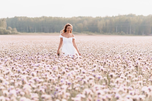 Beautiful happy woman in a white dress in a field of flowers in summer in nature