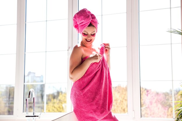 A beautiful and happy woman with a body and hair wrapped in a pink towel and with pink patches