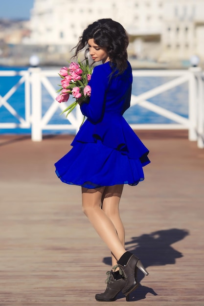 Beautiful happy woman with curly brunette hair dancing and holding a bouquet of pink tulips