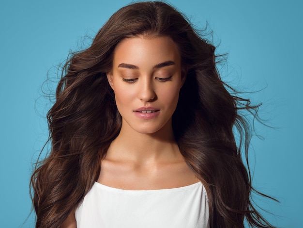 Beautiful happy woman with long hair in white dress over color blue background.Young model portrait