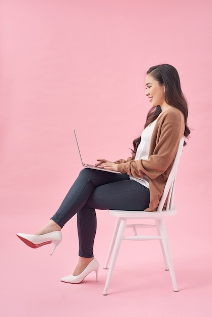 Beautiful and happy woman working with a laptop, isolated over pink background