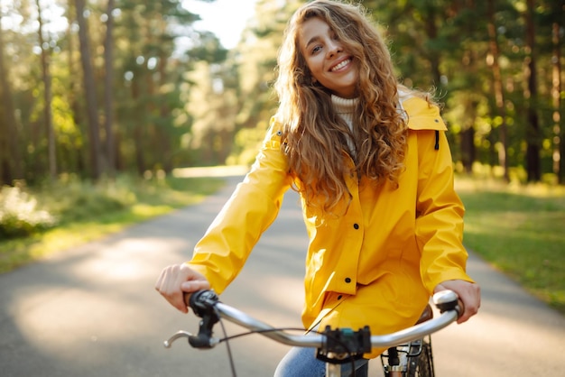 秋の公園で自転車に乗って黄色のコートを着た美しい幸せな女性秋のファッション、自然の概念