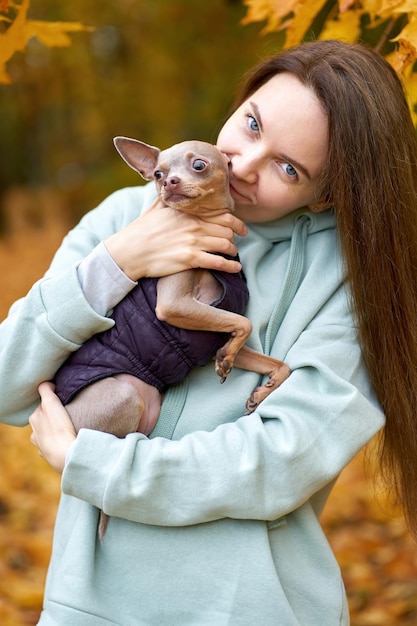 写真 美しい幸せなウォーワンは秋の公園で彼女の犬のおもちゃのテリアにキスを抱きしめます