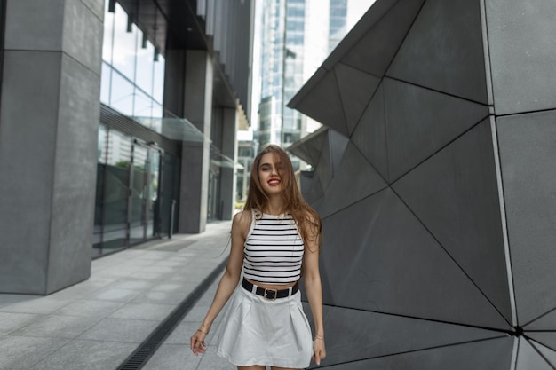 Foto modello di bella giovane ragazza castana felice in abiti casual moda estate cammina per strada vicino a edifici moderni