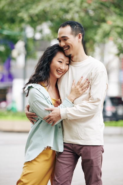 Photo beautiful happy young chinese woman hugging boyfriend when they are standing outdoors