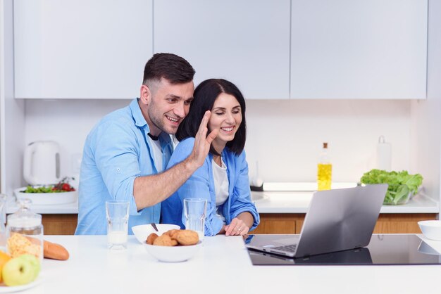 Foto bella giovane coppia felice che fa colazione a casa e usa il portatile in cucina a godersi il tempo libero