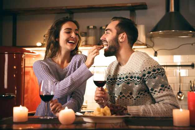 Belle giovani coppie felici che trascorrono insieme una serata romantica a casa, bevendo vino rosso, alimentando