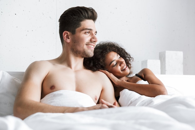 Beautiful happy young multiethnic couple relaxing in bed under blanket