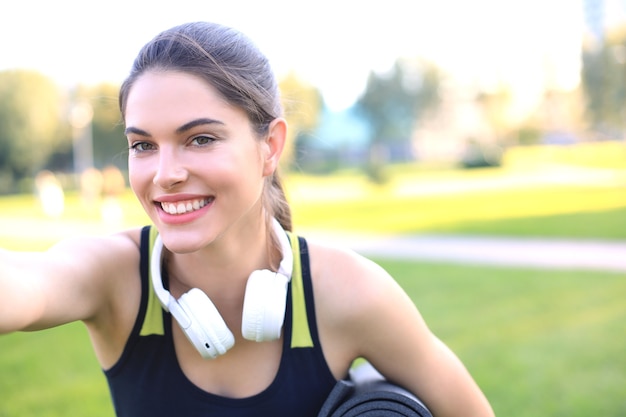都市公園でフィットネスラグを保持している美しい幸せな若いスポーツ女性。