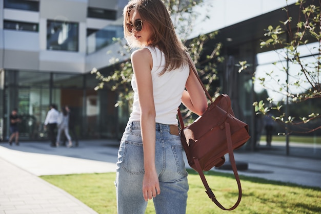 Beautiful, happy young student girl with backpack near the campus of university. Education and leisure concept