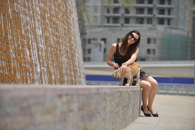 beautiful happy young  woman in black dress with cute small dog puppy have fun on street