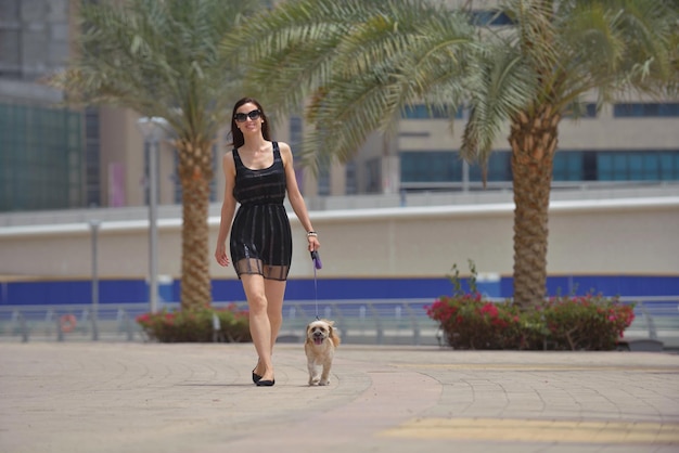 beautiful happy young  woman in black dress with cute small dog puppy have fun on street