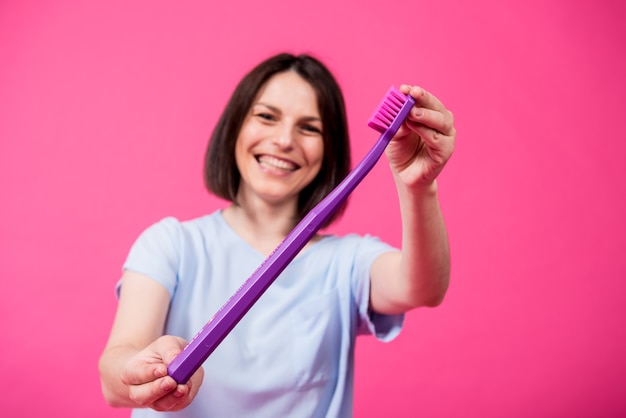 Beautiful happy young woman with big toothbrush on blank pink background