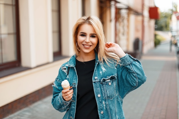 Foto bella giovane donna felice con un sorriso e un buon umore con gelato in jeans vestiti a piedi in città