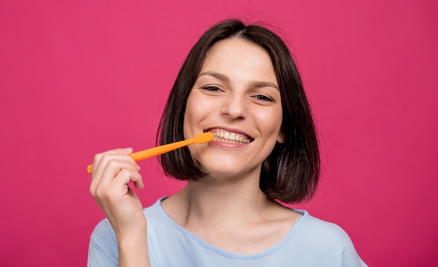 Beautiful happy young woman with toothbrush on blank pink background