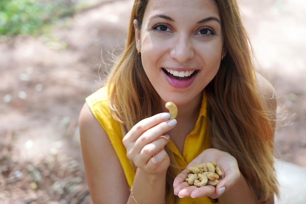 Beautiful healthy girl eating cashew nuts in the park Looks st camera